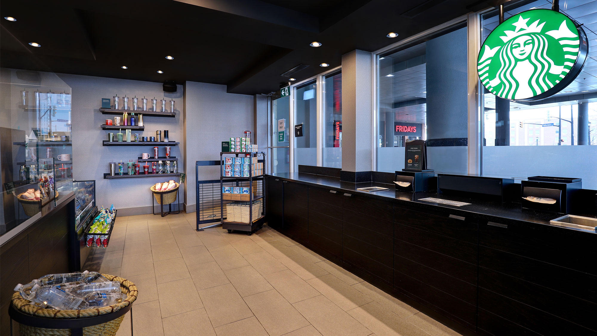 Starbucks café in hotel lobby with bright seating, food and drinks at the counter, and shelves of coffee products.